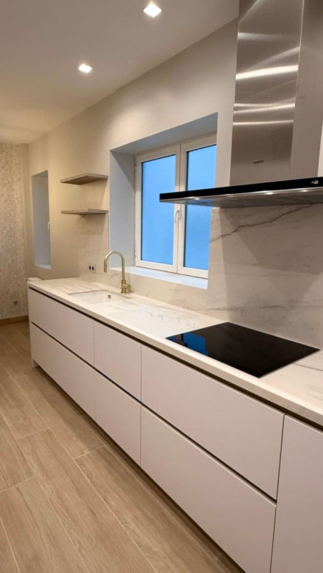 White kitchen with a marble worktop, a gold tap and floating timber shelves under the window